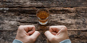 A person with fists clenched, struggling to resist the alcoholic drink in front of them.
