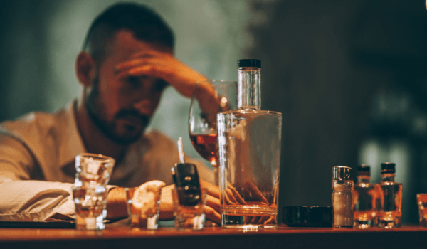 man with empty bottle and shot glasses - depression and alcoholism
