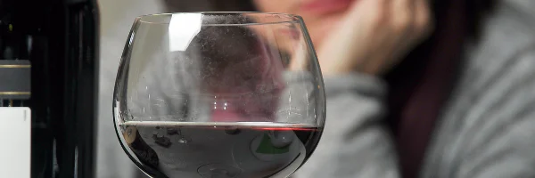 a glass of red wine - unhappy woman in background - seek alcohol rehab Exeter