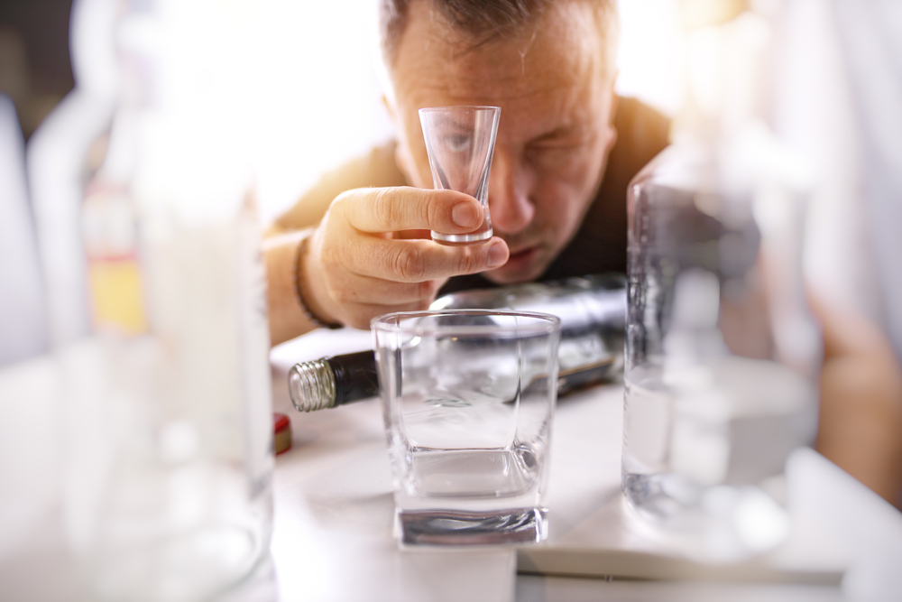Man looking at a shot glass, craving alcohol