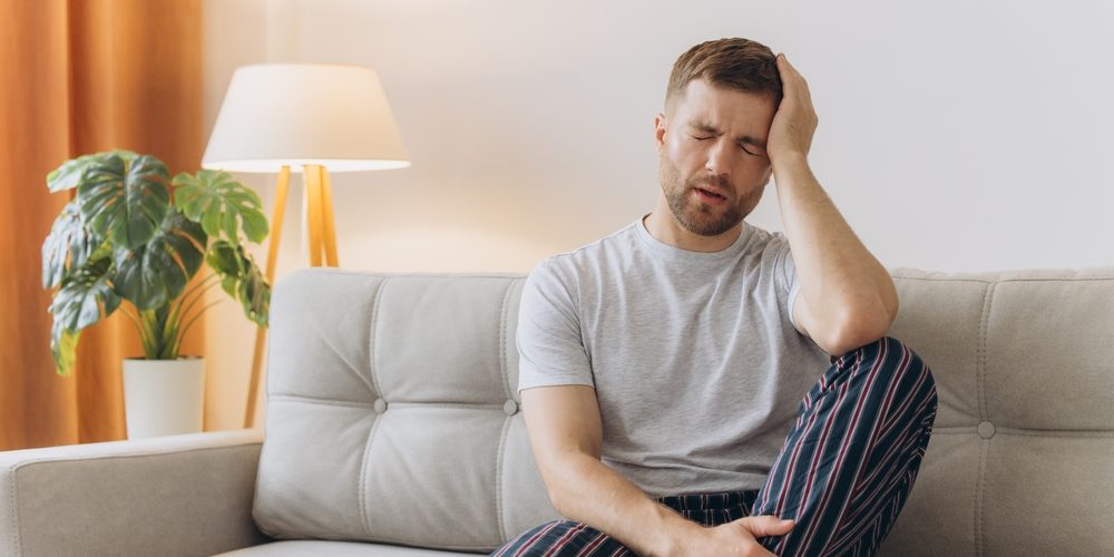 Young,Man,Suffering,From,Headache,At,Home,,Touching,His,Temples, A man hungover