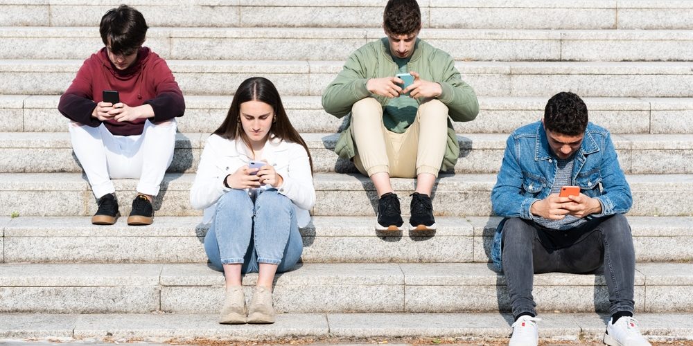 Teenager,Friends,Sitting,On,Stairs,And,Using,Their,Phones.,Digital Dopamine addiction shown in doom scrolling